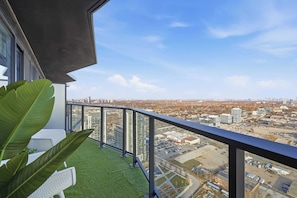A balcony with a view of a cityscape, including buildings and a parking lot. - Bright Condo, Skyline Views & Balcony | Parking (Toronto)