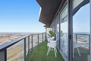Uma varanda com vista para a paisagem urbana, duas cadeiras brancas e um vaso de planta.