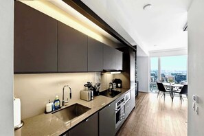 A modern kitchen with a built-in oven, a sink, and a dining area with a view of the city. - Downtown 1BR Urban Comfort Steps from it All (Toronto)