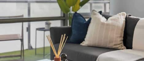 A modern living room with a glass coffee table, a sofa with cushions, a large window, and a potted plant.