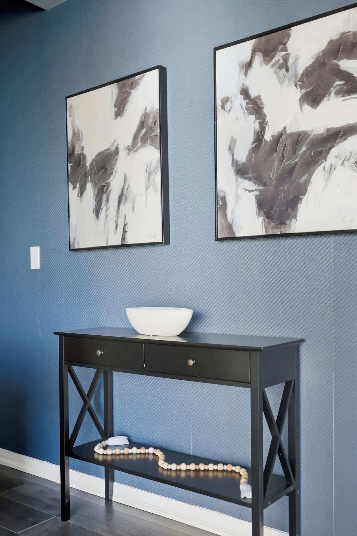 A room with a dark wooden console table, a white bowl, and abstract paintings on the wall.