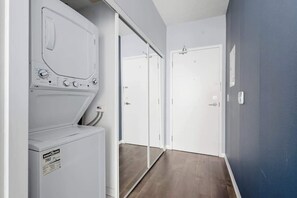 A laundry area with a front-loading washer and dryer, a hallway with a sliding door, and a blue wall. - Designer Skyline Retreat 2BR w Skyline Terrace! (Toronto)