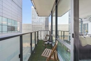 A balcony with a view of high-rise buildings, a small table with chairs, and a potted plant. - Designer Skyline Retreat 2BR w Skyline Terrace! (Toronto)