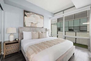 A modern hotel room with a large bed, a nightstand with a lamp, a painting above the bed, and a view through the window. - Designer Skyline Retreat 2BR w Skyline Terrace! (Toronto)