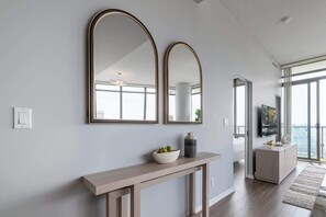 A modern interior with a wooden console table, two large mirrors, a vase, and a television on a stand. - Modern 2BR Haven, Luxury Stay in Financial Dist (Toronto)