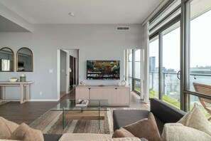 Ein modernes Wohnzimmer mit großem Flachbildfernseher, einem Glastisch und einer Couch.