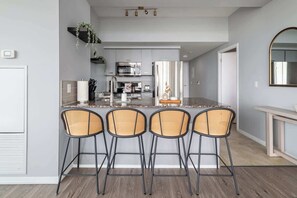 A modern kitchen with a central island, stainless steel appliances, and a seating area with wicker chairs. - Modern 2BR Haven, Luxury Stay in Financial Dist (Toronto)