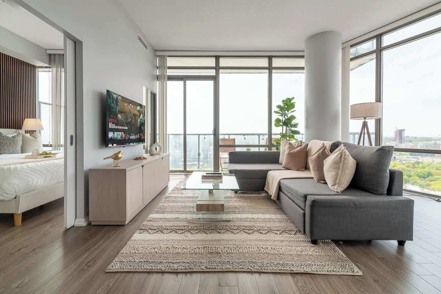 Een moderne woonkamer met een bank, een televisie en een groot raam met uitzicht op de stad.