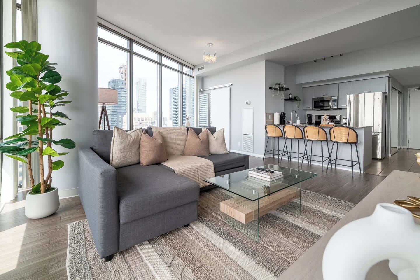 A modern living room with a sofa, a glass coffee table, and a large window offering a city view.