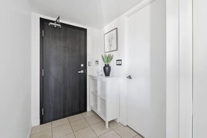 A hallway with a dark wooden door, a white console table with a vase, and a framed picture on the wall. - Chic Metropolitan Suite Skyline Views & Parking | Parking Available (Toronto)