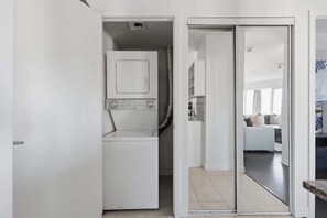 A laundry room with a washing machine and dryer, a hallway leading to a living area with a sofa and a coffee table. - Chic Metropolitan Suite Skyline Views & Parking | Parking Available (Toronto)