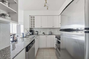 A modern kitchen with white cabinets, stainless steel appliances, and a granite countertop. - Chic Metropolitan Suite Skyline Vistas & Parking (Toronto)
