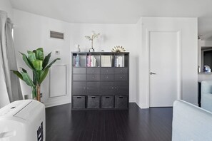 A modern room with a dark wood floor, a white door, a grey bookshelf, and a large green plant. - Chic Metropolitan Suite Skyline Vistas & Parking (Toronto)