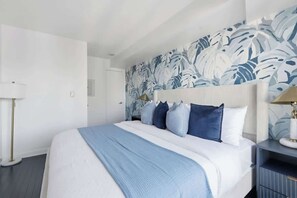 A hotel room with a large bed, a headboard with a leaf pattern, a bedside table with a lamp, and a floor lamp. - Chic Metropolitan Suite Skyline Views & Parking | Parking Available (Toronto)