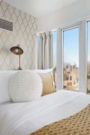 A bedroom with a large window, a bed with white bedding, a fluffy pillow, and a patterned wall. - Chic Metropolitan Suite Skyline Vistas & Parking (Toronto)