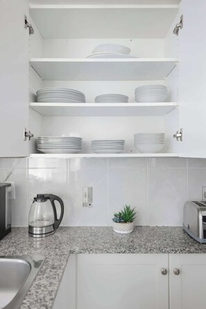 A kitchen with white cabinets, a granite countertop, a kettle, a toaster, and a potted plant. - Chic Metropolitan Suite Skyline Views & Parking | Parking Available (Toronto)