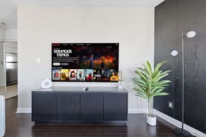 A modern living room with a flat-screen TV displaying a Netflix interface, a dark wood floor, a white console table, and a potted plant. - Chic Metropolitan Suite Skyline Vistas & Parking (Toronto)