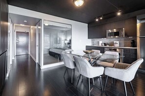 A modern kitchen with a glass dining table, stainless steel appliances, and a sliding glass door leading to a bedroom. - Elevated Downtown 3BR w Views & Free Parking (Toronto)