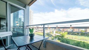A balcony with a table and chair, a potted plant, and a view of a cityscape with buildings and greenery. - Elevated Downtown Living Luxe 3BR w Views! (Toronto)