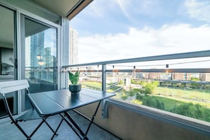 A balcony with a table and chair, a potted plant, and a view of a cityscape with buildings and greenery. - Elevated Downtown Living Luxe 3BR w Views! (Toronto)