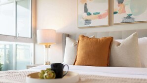 A neatly made bed with a white comforter, a mustard-colored pillow, and a black mug on a tray. - Elevated Downtown Living Luxe 3BR w Views! (Toronto)