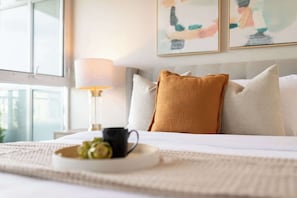 A neatly made bed with a white comforter, a mustard-colored pillow, and a black mug on a tray. - Elevated Downtown Living Luxe 3BR w Views! (Toronto)
