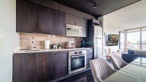 A modern kitchen with dark cabinetry, stainless steel appliances, and a glass dining table. - Elevated Downtown Living Luxe 3BR w Views! (Toronto)