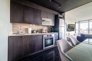 A modern kitchen with dark cabinetry, stainless steel appliances, and a glass dining table. - Elevated Downtown Living Luxe 3BR w Views! (Toronto)