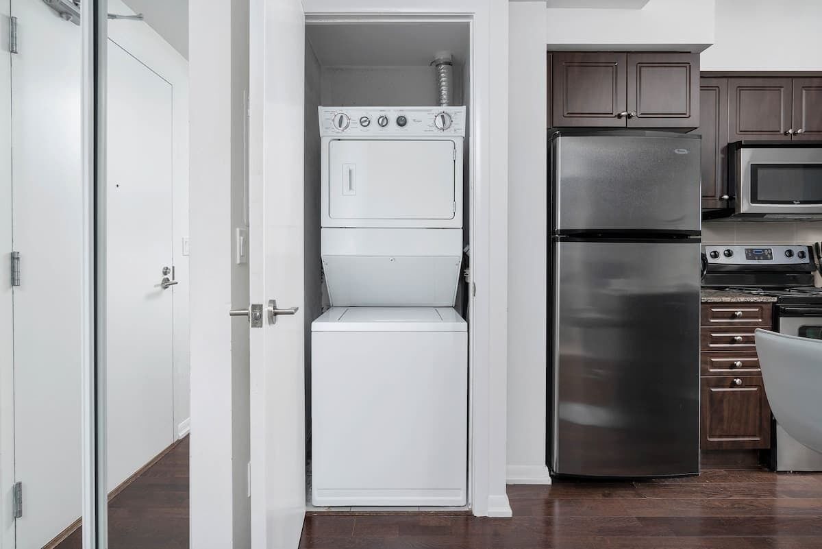 A compact kitchen with a built-in washer and dryer, a stainless steel refrigerator, and a microwave.