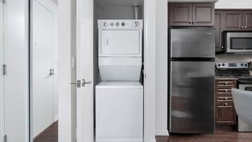A compact kitchen with a built-in washer and dryer, a stainless steel refrigerator, and a microwave.