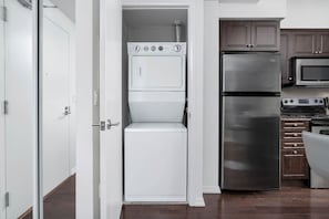 A compact kitchen with a built-in washer and dryer, a stainless steel refrigerator, and a microwave.