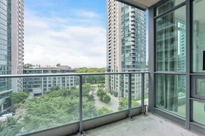 A high-rise building with multiple balconies, large windows, and a view of a green area with trees. - Chic Fort York Condo w Stunning Balcony Views | Parking Available (Toronto)