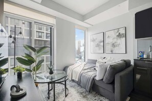 Ein modernes Wohnzimmer mit einer Couch, einem Glastisch und Blick auf die Stadt durch große Fenster.