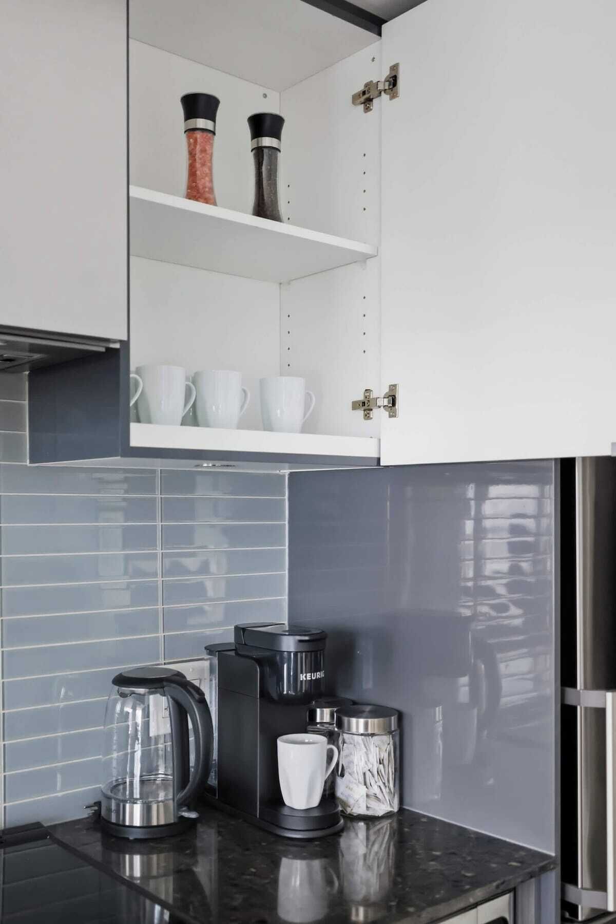 A modern kitchen with white cabinets, a black countertop, and a coffee maker.