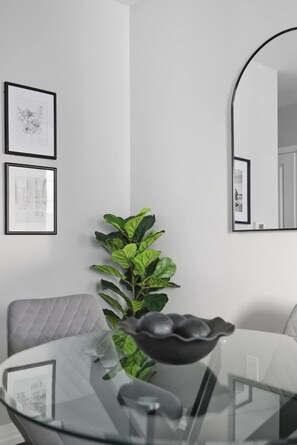Ein stilvolles Zimmer mit Glastisch, einer Couch, einer Topfpflanze und gerahmten Bildern an der Wand.