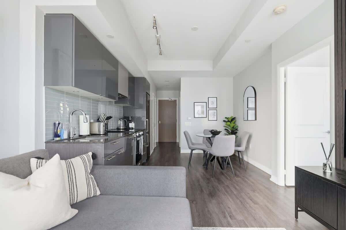 A modern kitchen with a dining area, grey sofa, and a small table with chairs.