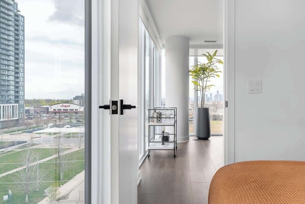 Habitación de hotel moderna con un ventanal grande, vistas a un paisaje urbano y una planta en la esquina.