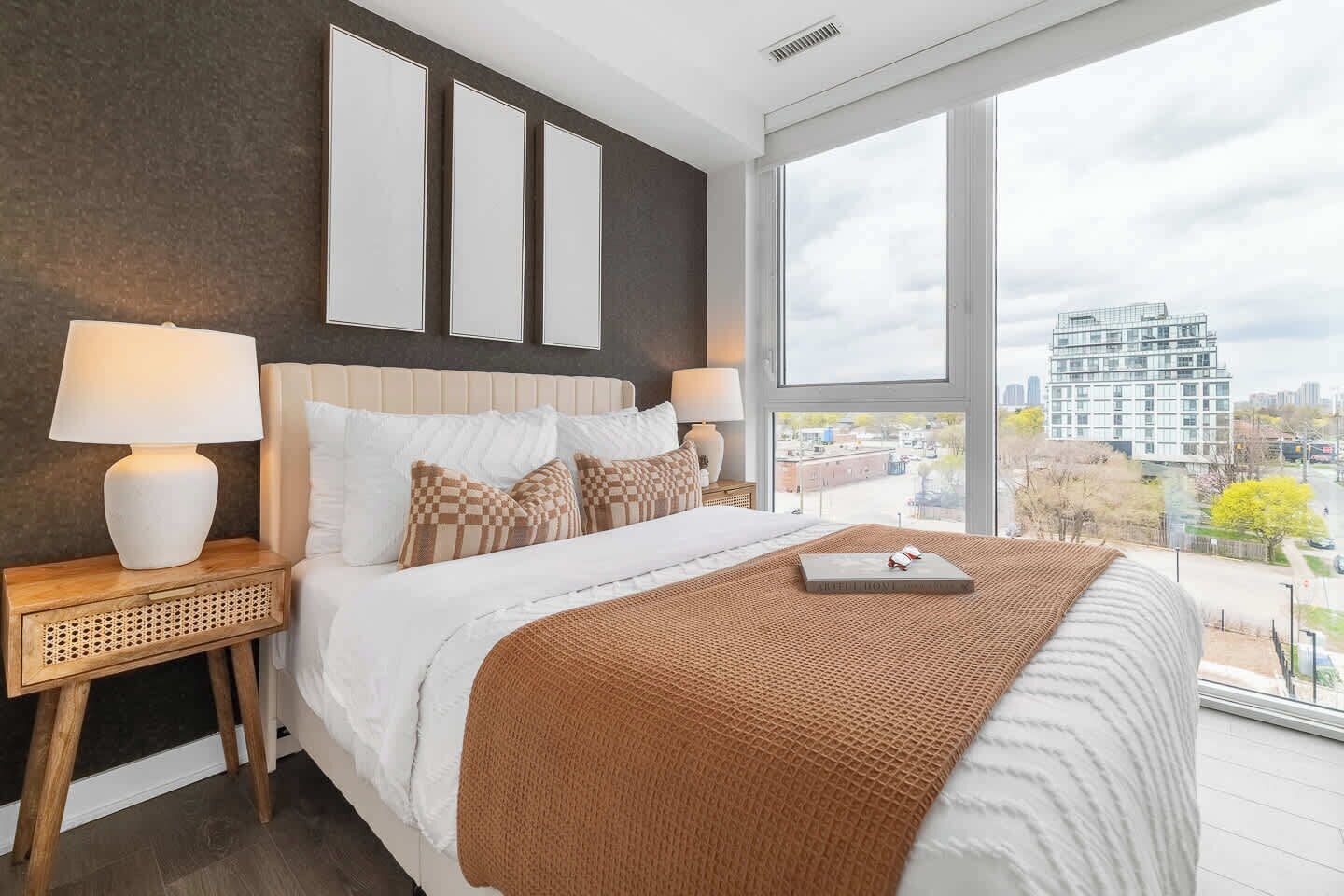 A modern bedroom with a large bed, two bedside tables, a view of the city through large windows, and a cityscape visible outside.