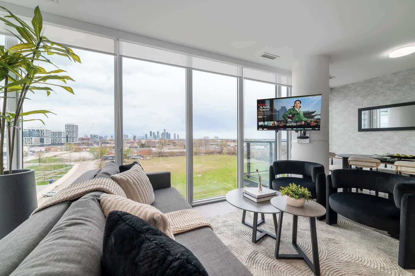 A modern living room with a large window, a flat-screen TV, a sofa, and a dining area.