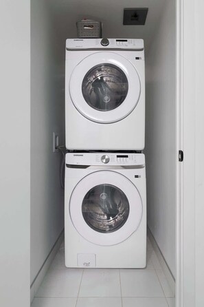 Dos lavadoras Samsung blancas apiladas en un pasillo estrecho con paredes blancas y piso de baldosas.