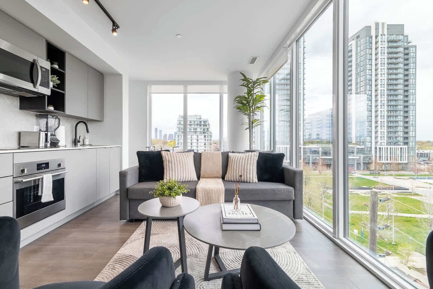 A modern living room with a grey sofa, a round coffee table, and a view of a cityscape through large windows.