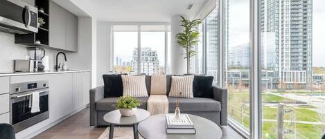 A modern living room with a grey sofa, a round coffee table, and a view of a cityscape through large windows.