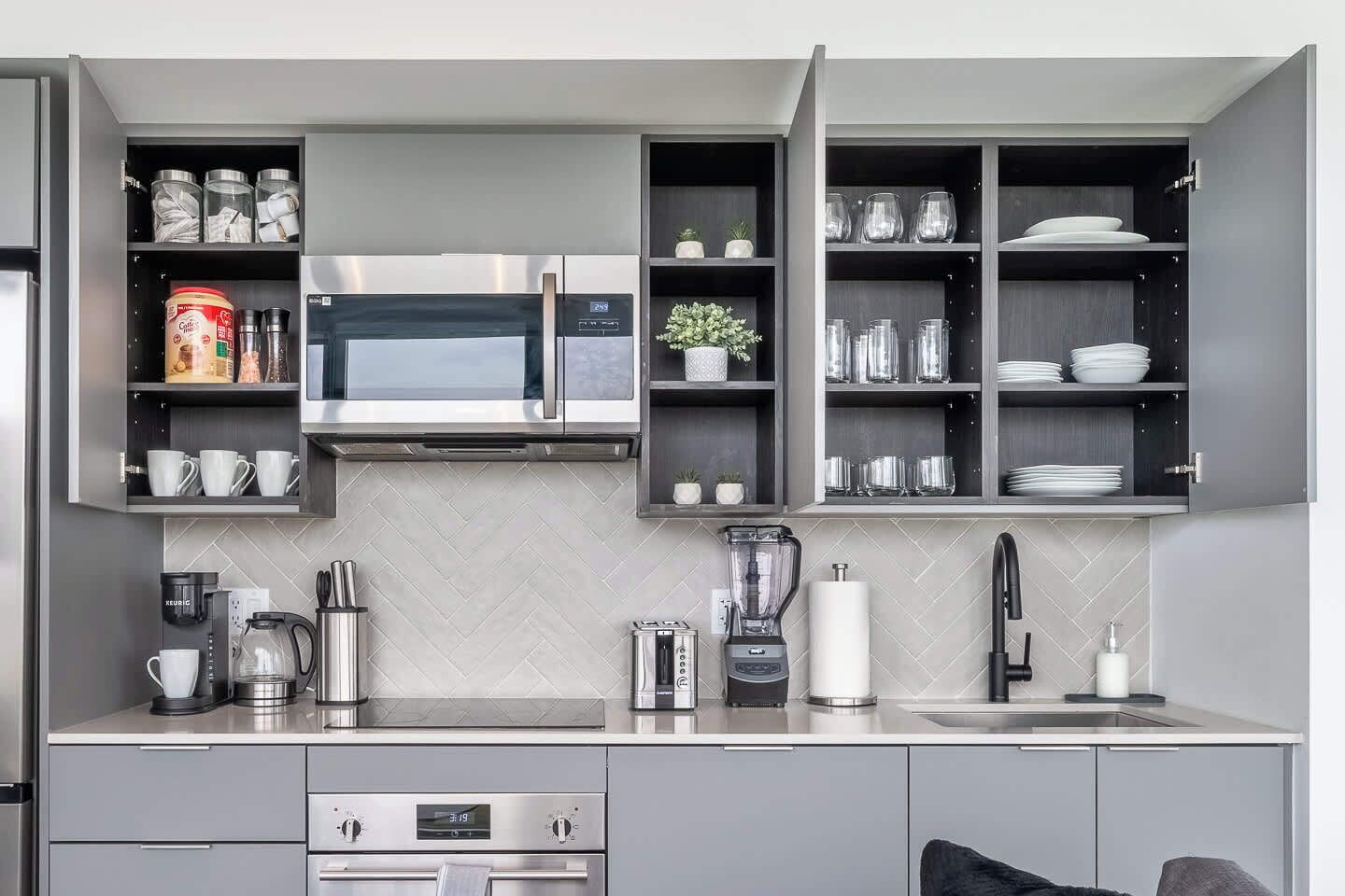 A modern kitchen with a built-in microwave, a coffee maker, and a blender on the countertop.