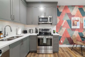 Eine moderne Küche mit grauen Schränken, Edelstahlgeräten und einem farbenfrohen geometrischen Wandmuster.