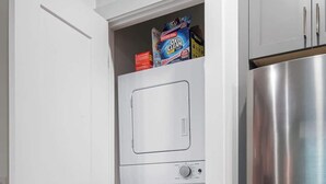 Eine kompakte Küche mit integrierter Waschmaschine und Trockner, einem Edelstahlkühlschrank und einer weißen Tür.