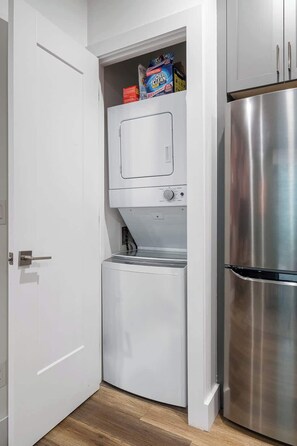 Eine kompakte Küche mit integrierter Waschmaschine und Trockner, einem Edelstahlkühlschrank und einer weißen Tür.