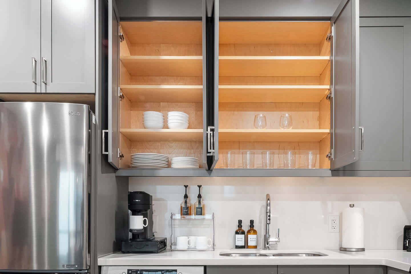 Eine Küche mit einem Edelstahl-Kühlschrank, offenen Schränken mit Regalen, einer Kaffeemaschine und einem Spülbecken.