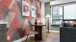 Ein modernes Wohnzimmer mit einer Wand mit geometrischem Muster, einem runden Tisch mit Stühlen, einer Couch und einer Lampe.