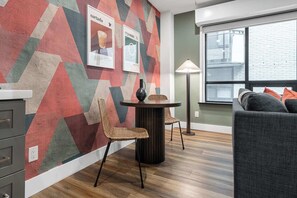 Ein modernes Wohnzimmer mit einer Wand mit geometrischem Muster, einem runden Tisch mit Stühlen, einer Couch und einer Lampe.