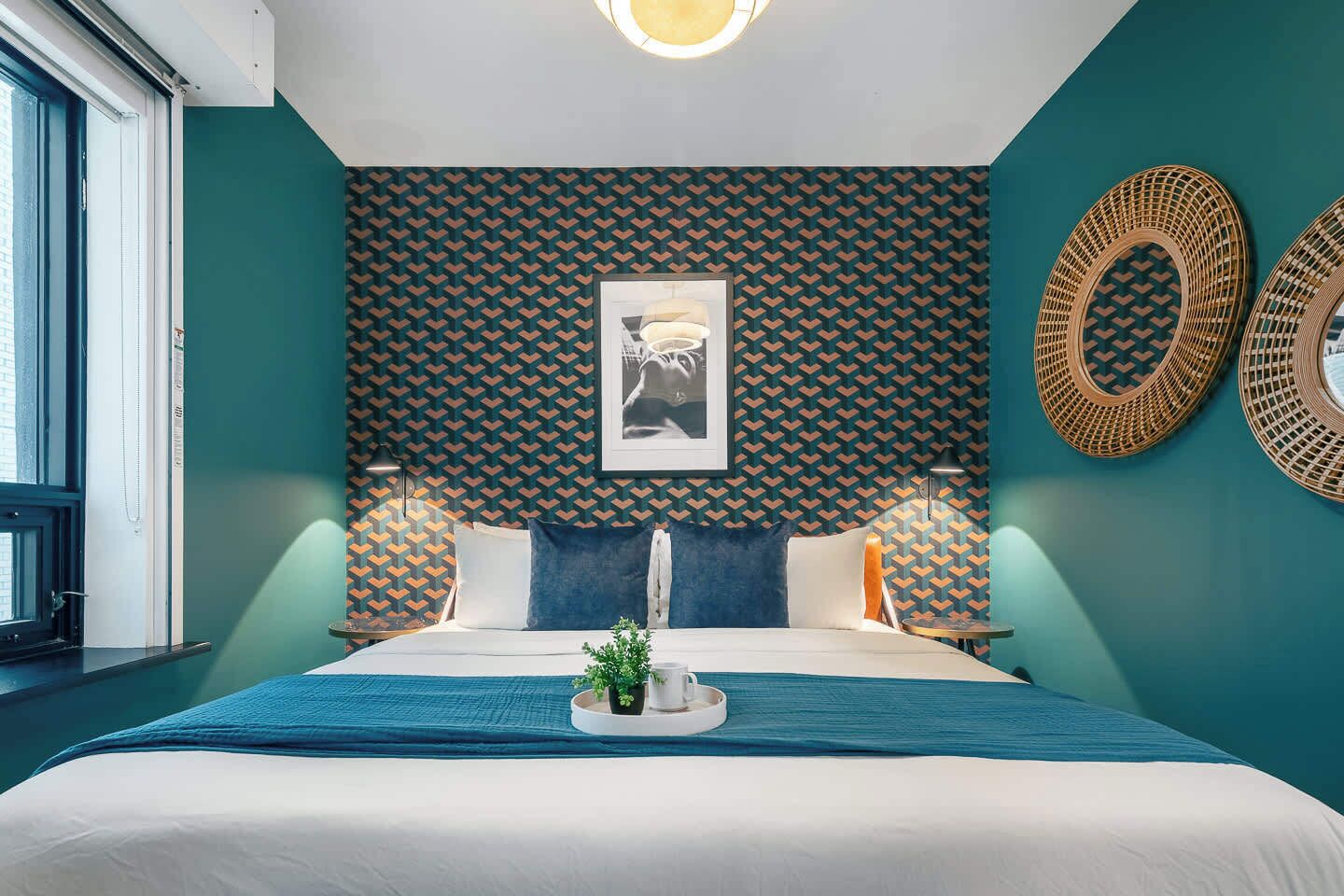 Une chambre d’hôtel comprenant un lit, une fenêtre, un mur orné d’un motif géométrique et deux éléments décoratifs fixés au mur.